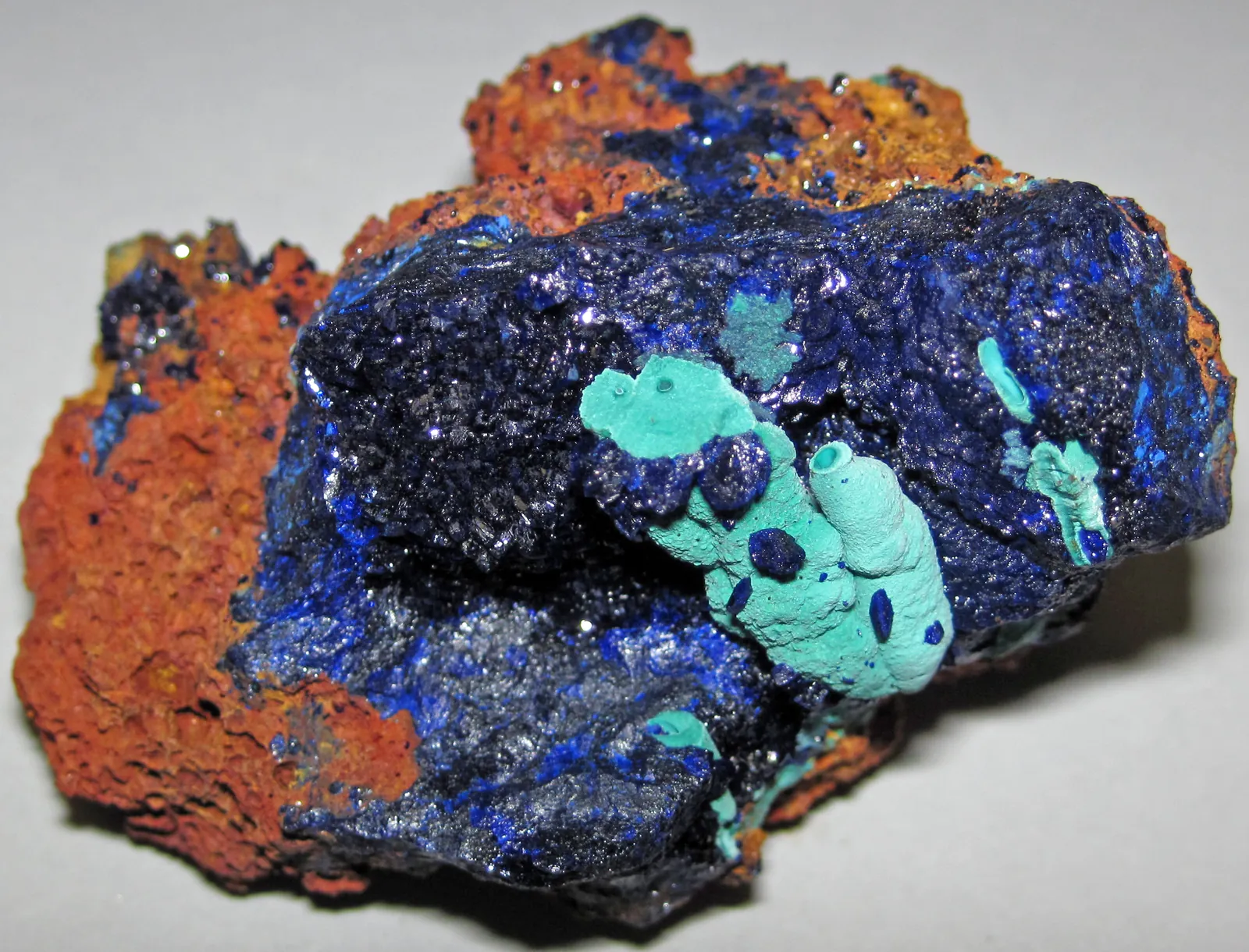 Hand specimen of rust-orange gossan partly covered by deep blue azurite and pale green malachite